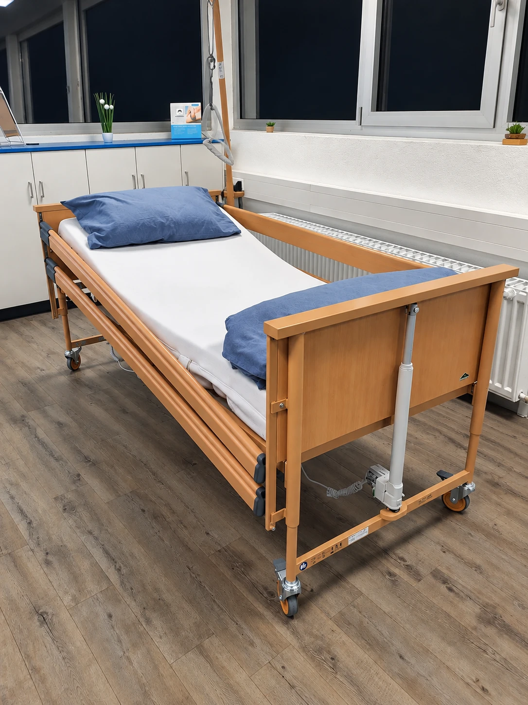 Pflegebett in Buche-Optik mit Seitengittern, angehobenem Rückenteil, Aufrichter mit Haltegriff und Hubmotor am Fußteil